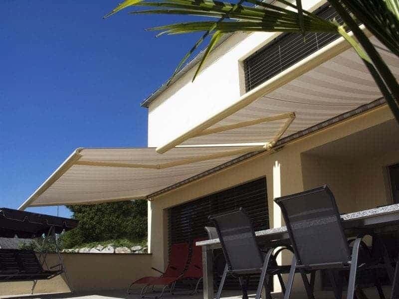 Beżowa markiza tarasowa rozłożona nad stołem i krzesłami na tarasie domu